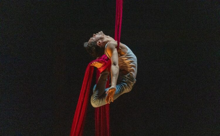 man doing aqrobatic routine hanging on red rope
