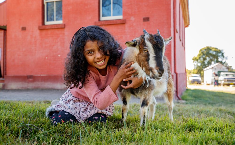 Aishi Wijesekera with a goat in front of the fence at Rouse Hill House & Farm (c) James Horan for Museums of History NSW 