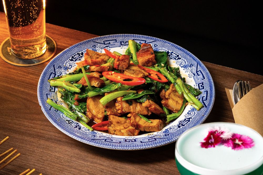 Crispy pork belly stir fry with Chinese broccoli and chilli on a blue and white plate at M Bar Sydney