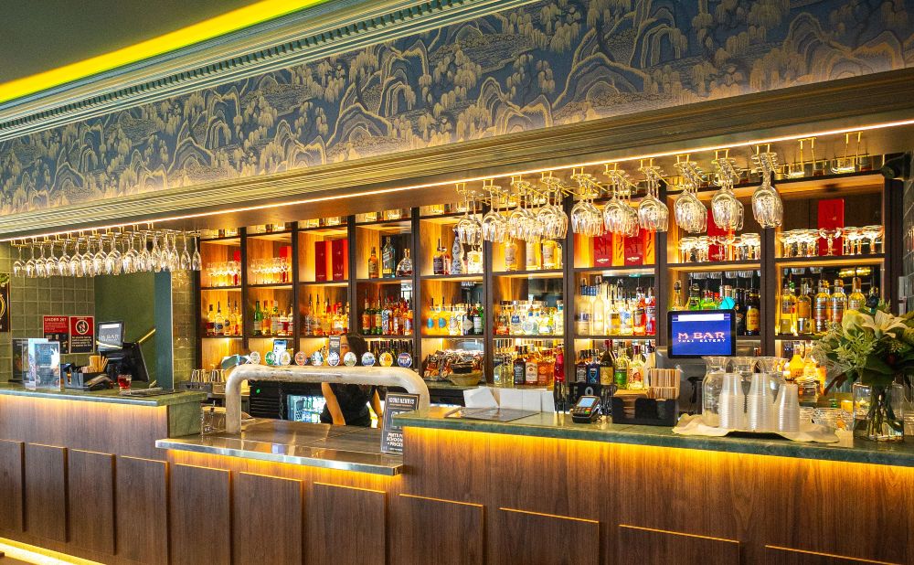 The lit bar at M Bar Sydney with hanging glassware and blue landscape wallpaper above the spirits shelves