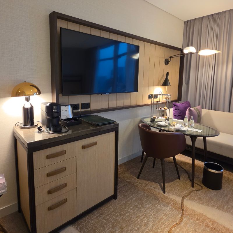 Sofitel Sydney Darling Harbour room featuring flatscreen TV on timber panelled wall, coffee machine, and work desk with natural light from window