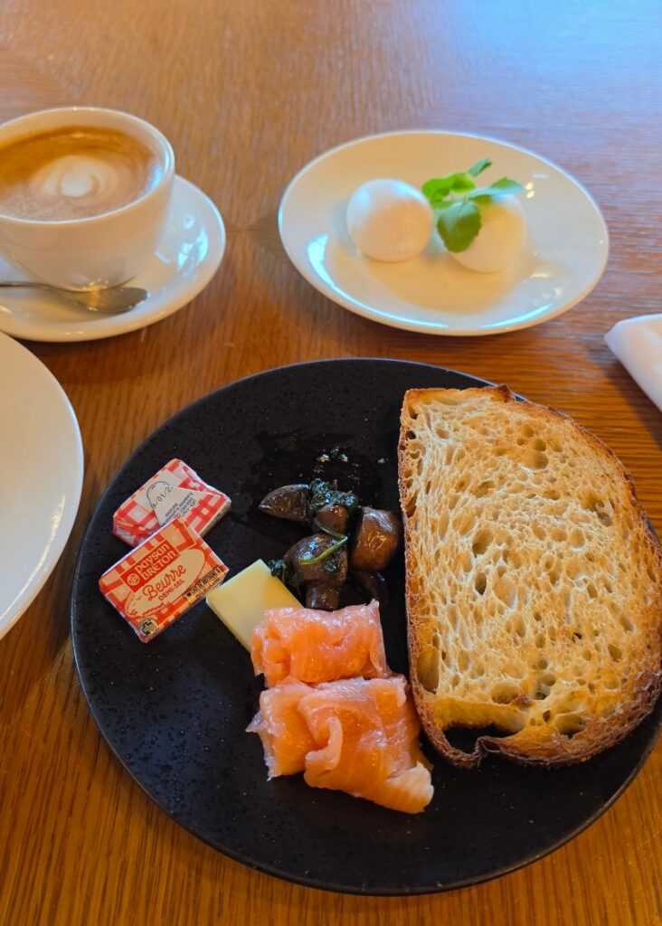 Sofitel Sydney Darling Harbour breakfast spread including cappuccino, poached eggs, crusty sourdough toast, smoked salmon, sautéed mushrooms, and French Breton butter